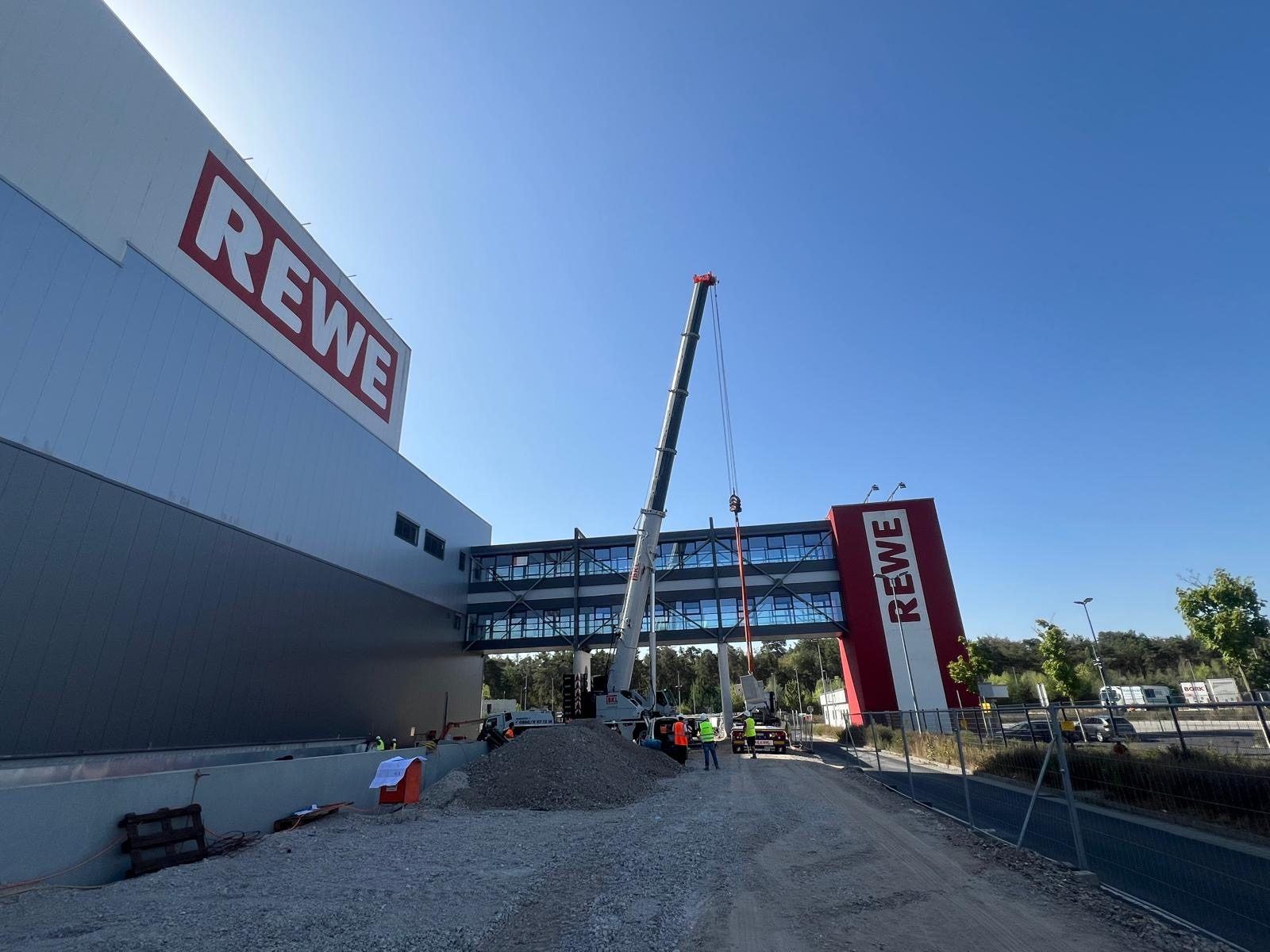 Mobilkran hebt ein Fertigteil vor dem REWE-Gebäude ein